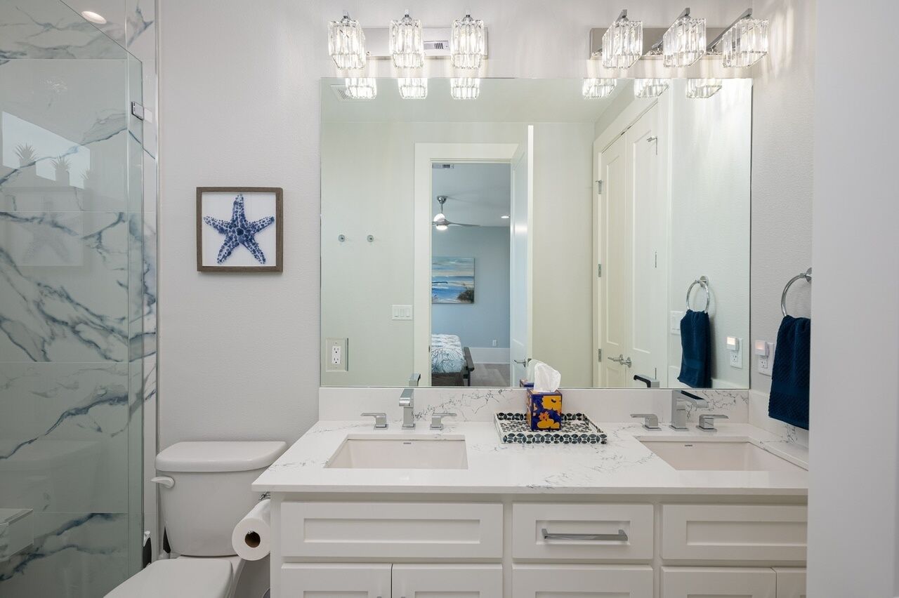 A modern bathroom with a white marble backsplash, a double sink vanity, and a large mirror with overhead lighting.