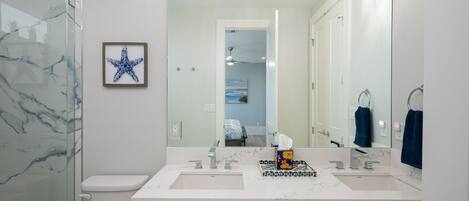 A modern bathroom with a white marble backsplash, a double sink vanity, and a large mirror with overhead lighting.