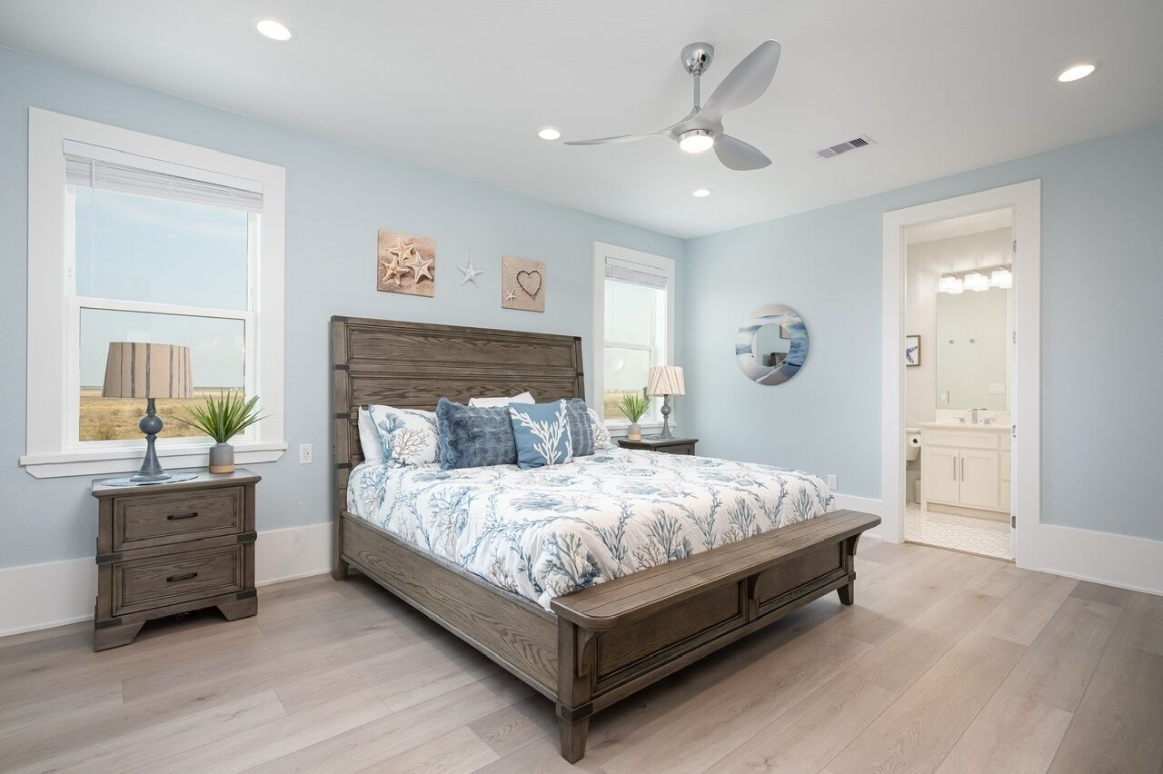 A bedroom with a wooden bed, two bedside tables, a ceiling fan, and a view of the bathroom.
