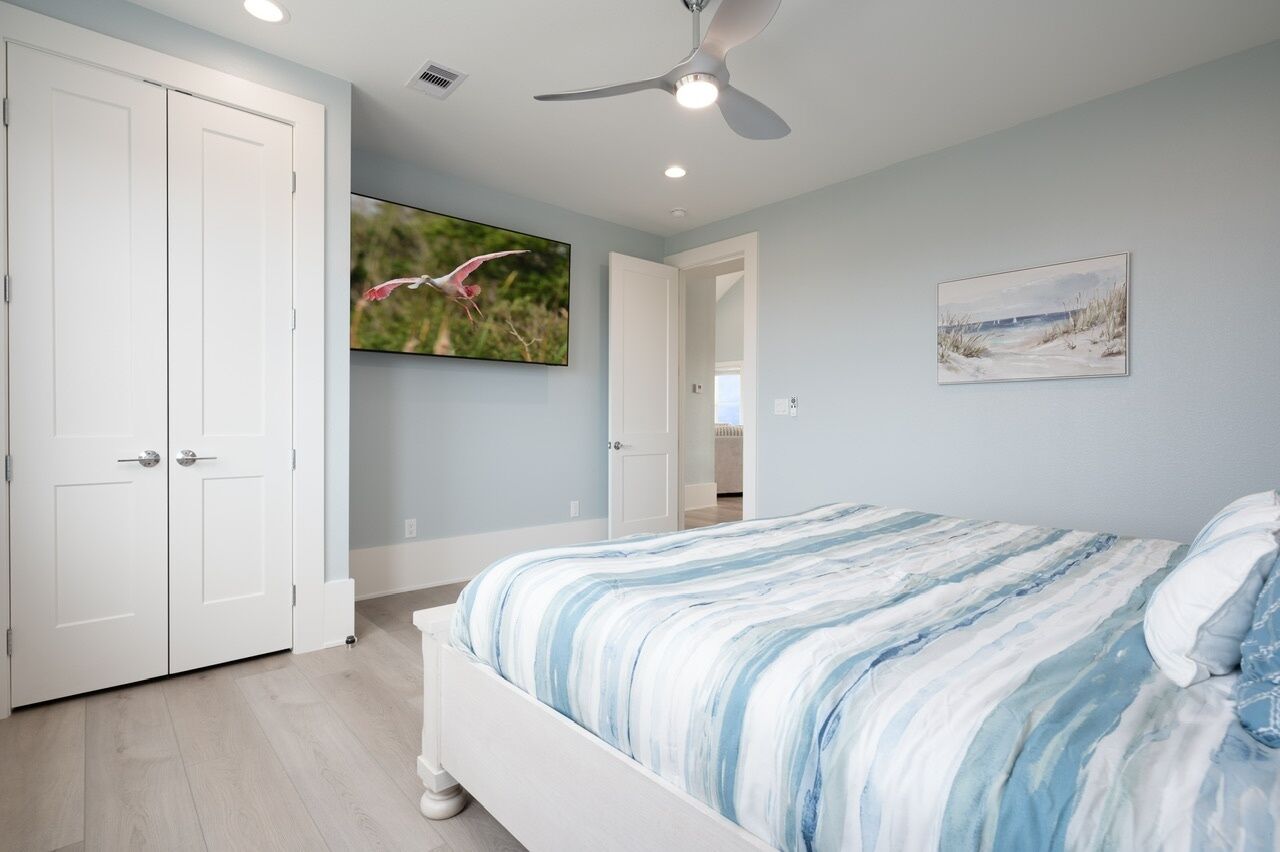 A bedroom with a bed, a ceiling fan, a TV, and a door.