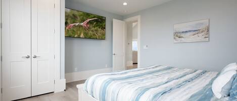 A bedroom with a bed, a ceiling fan, a TV, and a door.