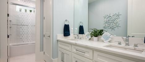 A modern bathroom with a large mirror, two sinks, and a shower area.