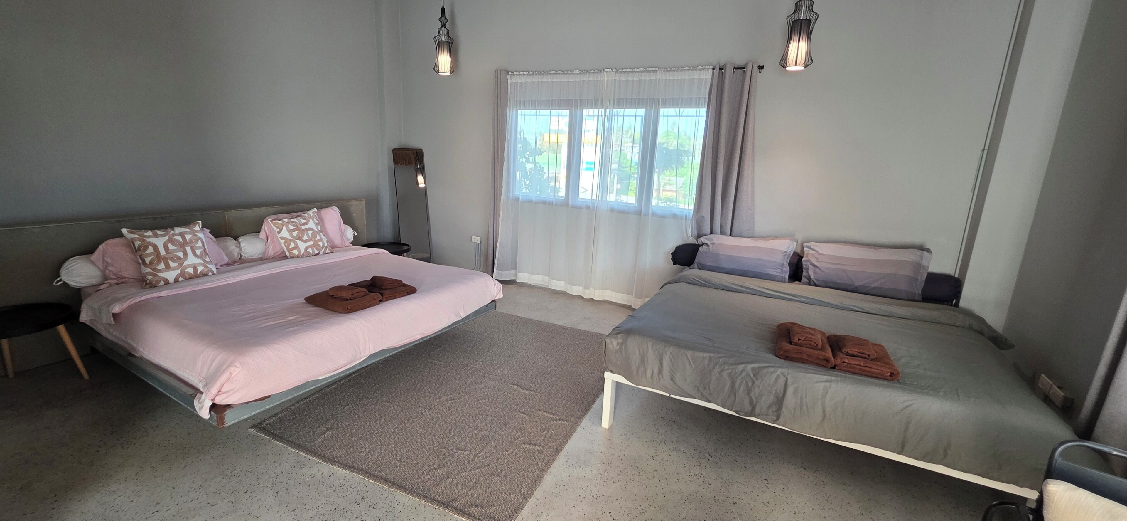 A bedroom with two beds, a bedside table, a floor lamp, and a window with curtains.