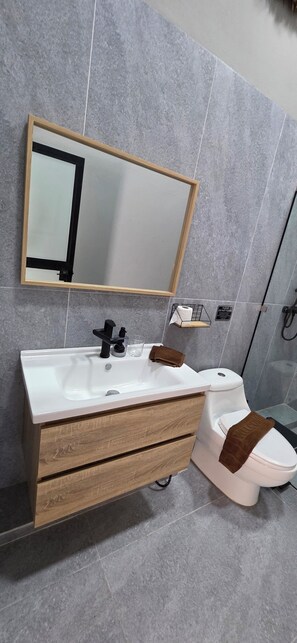 Et badeværelse med en hvid vask, trækommode, et spejl og et toilet.