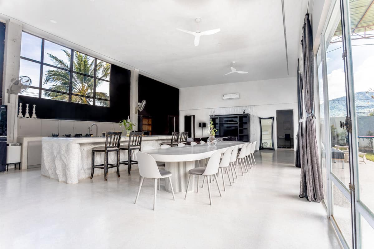 A spacious kitchen with a long island, white chairs, and a large window with a view of palm trees.