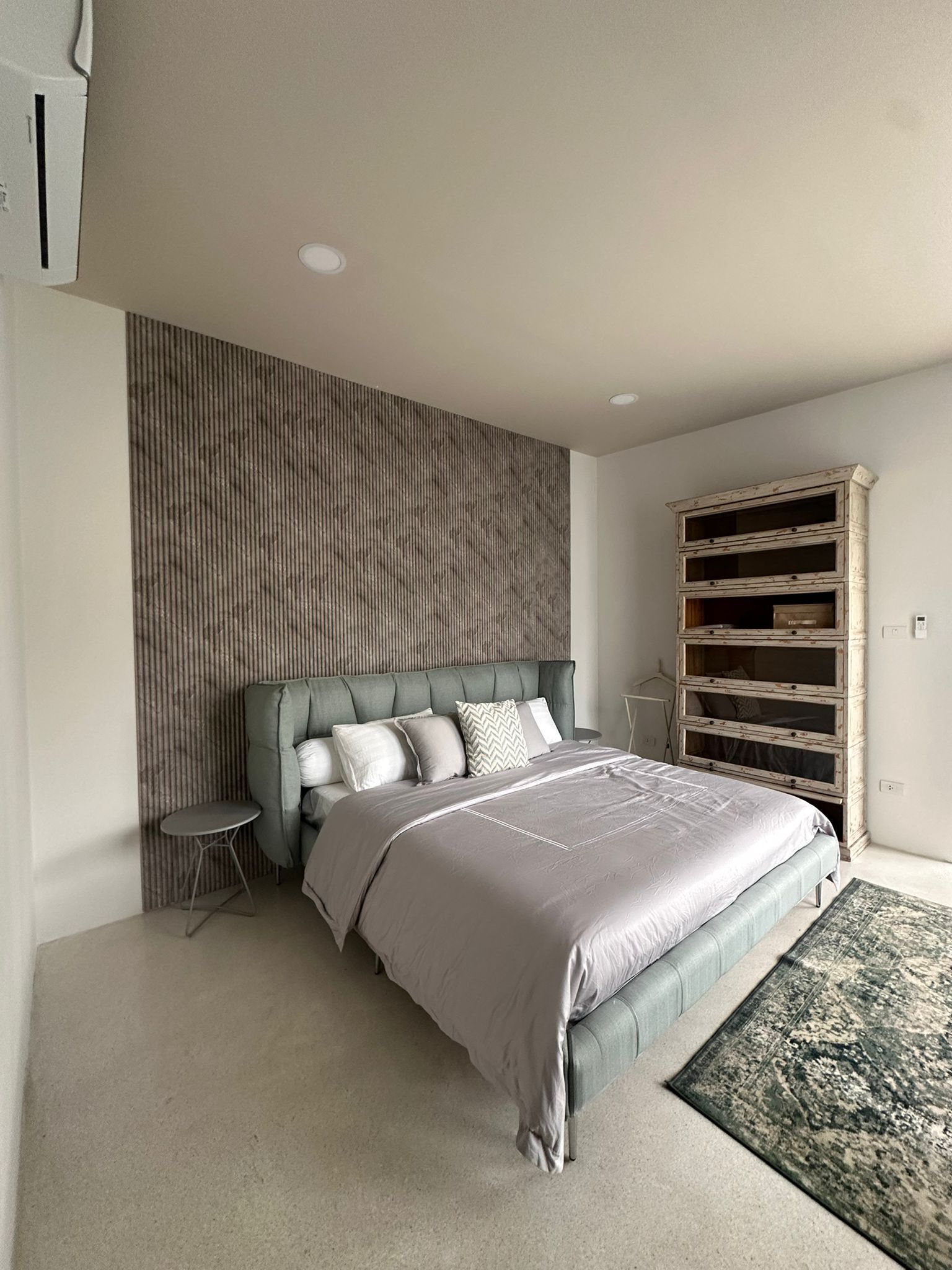 A modern bedroom with a large bed, a small side table, a built-in wardrobe, and a textured wall.