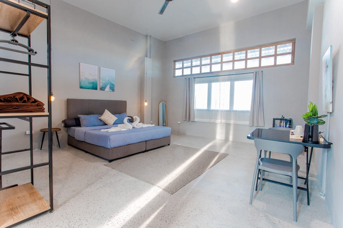 A modern bedroom with a bed, a desk, and a large window.
