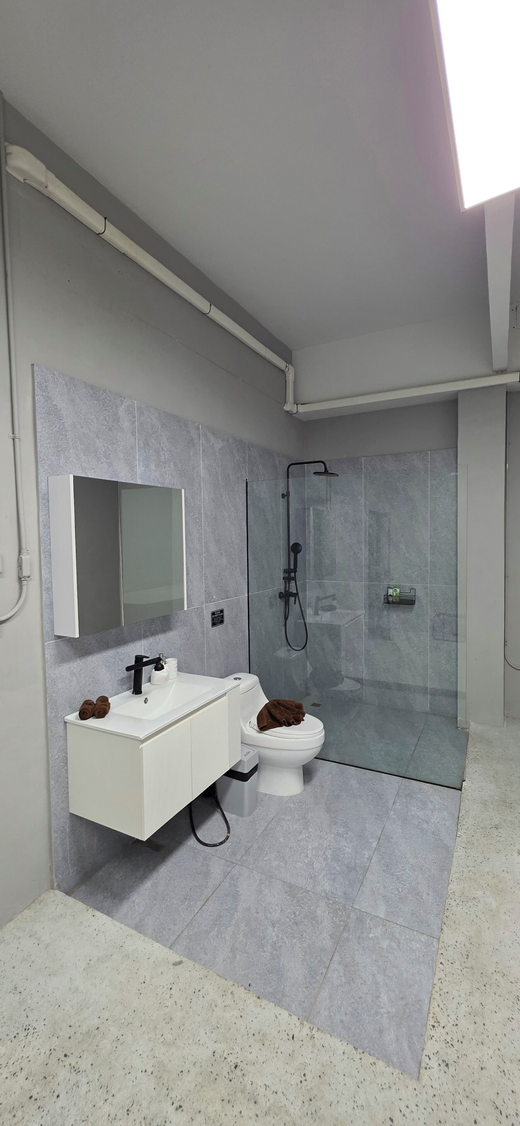 A modern bathroom with a white vanity, a toilet, a glass shower enclosure, and a visible pipe on the ceiling.