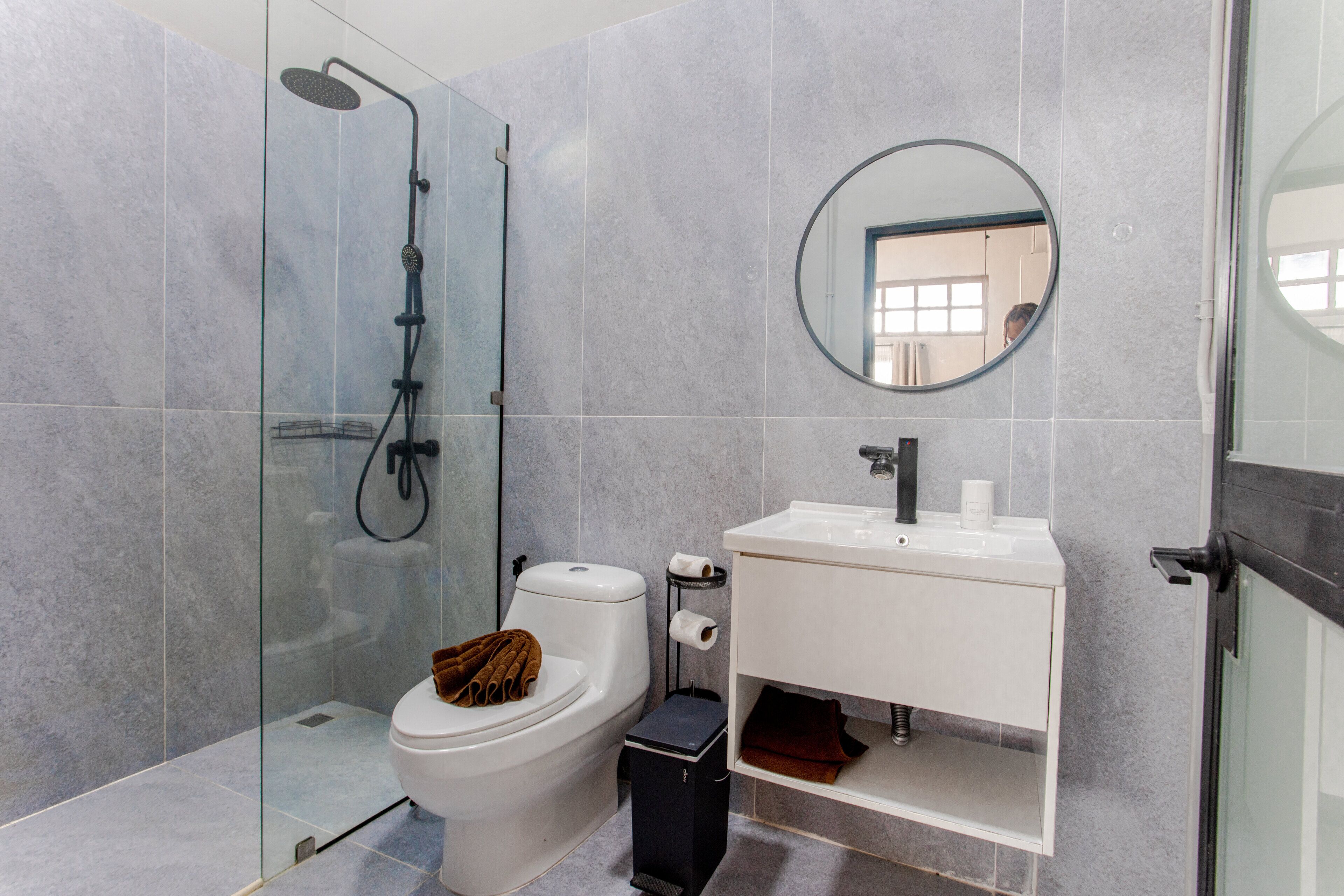 Un baño moderno con ducha de vidrio, inodoro blanco y lavamanos blanco con espejo arriba.