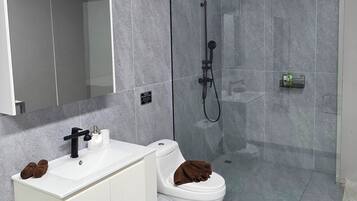 A modern bathroom with a white vanity, a toilet, and a glass-enclosed shower.