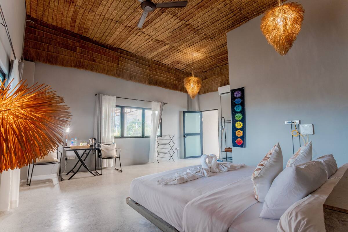 A hotel room with a bed, a desk, and a chair. There is a ceiling fan and a wall-mounted light fixture.