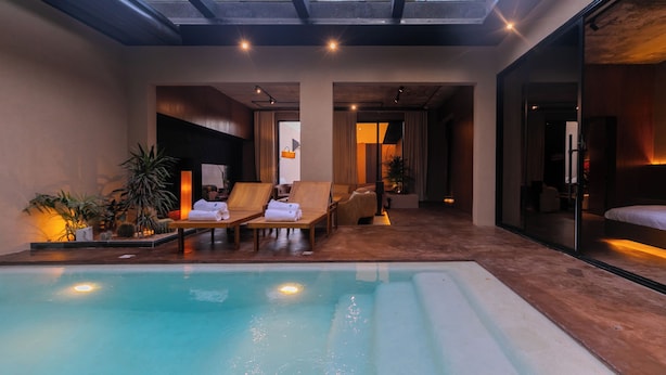 A modern indoor swimming pool area with lounge chairs, a glass-enclosed bedroom, and a skylight. - Portal Chalets With Private Pool-Al Arid (Riyadh)