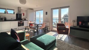 A modern living room with a green sofa, a dining area with a table and chairs, a kitchen with a microwave and cabinets, and a TV on a stand. - The Beach Retreat Apartment, Balcony views of shanklin bay. (Shanklin)