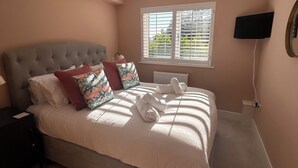 A bedroom with a bed, a bedside table, a lamp, a ceiling light, a window with blinds, and a TV mounted on the wall. - The Beach Retreat Apartment, Balcony views of shanklin bay. (Shanklin)