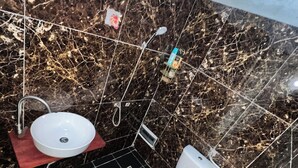 Ein Badezimmer mit Waschbecken, Toilette und Dusche. Der Boden ist mit Fliesen belegt, und die Wände sind mit einem marmorähnlichen Material verkleidet.