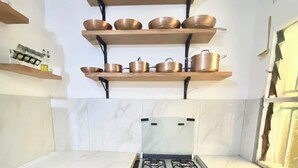 Eine kleine Küche mit Gaskochfeld, Backofen und zwei Regalen darüber, auf denen Kochutensilien stehen.