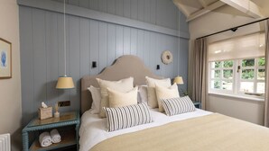 Un dormitorio con una cama grande, dos mesitas de noche, un ventanal con cortinas y una lámpara fijada a la pared.