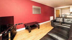 A modern living room with a red wall, a black leather sofa, a wooden coffee table, and a flat-screen TV. - 2 Bedroom Apartment 4 Guests (Newcastle-upon-Tyne)