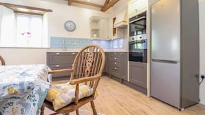 Una cocina con una silla de madera, una cama, un reloj y un refrigerador.