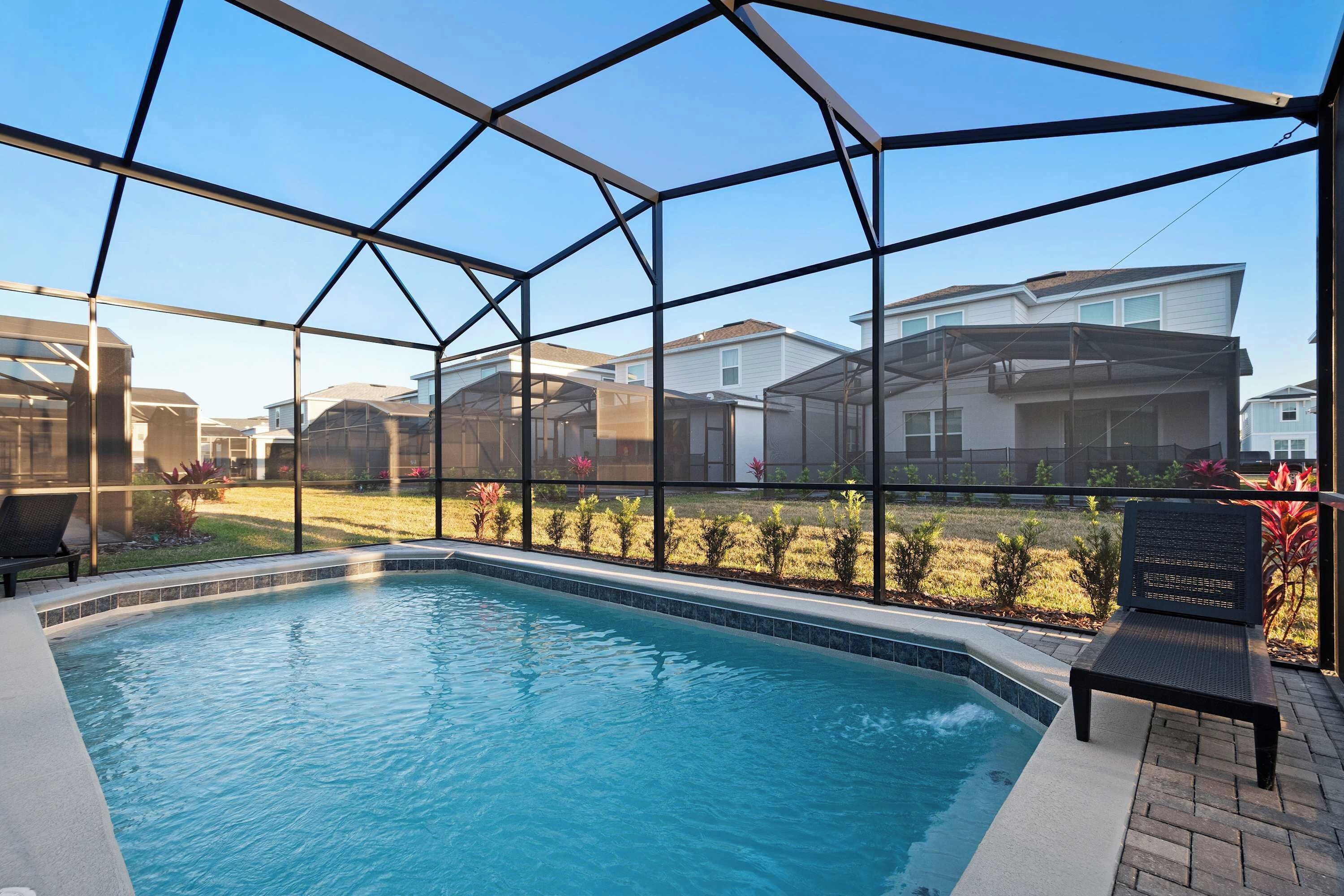 Une piscine dotée d’une enceinte en verre, entourée d’un patio agrémenté d’un banc.