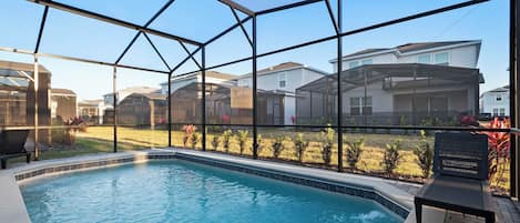 A swimming pool with a glass enclosure, surrounded by a patio area with a bench.
