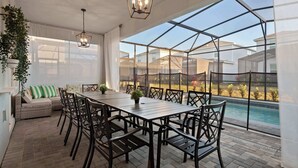 Un patio couvert avec une table et des chaises, un coin salon confortable et une vue sur une piscine.