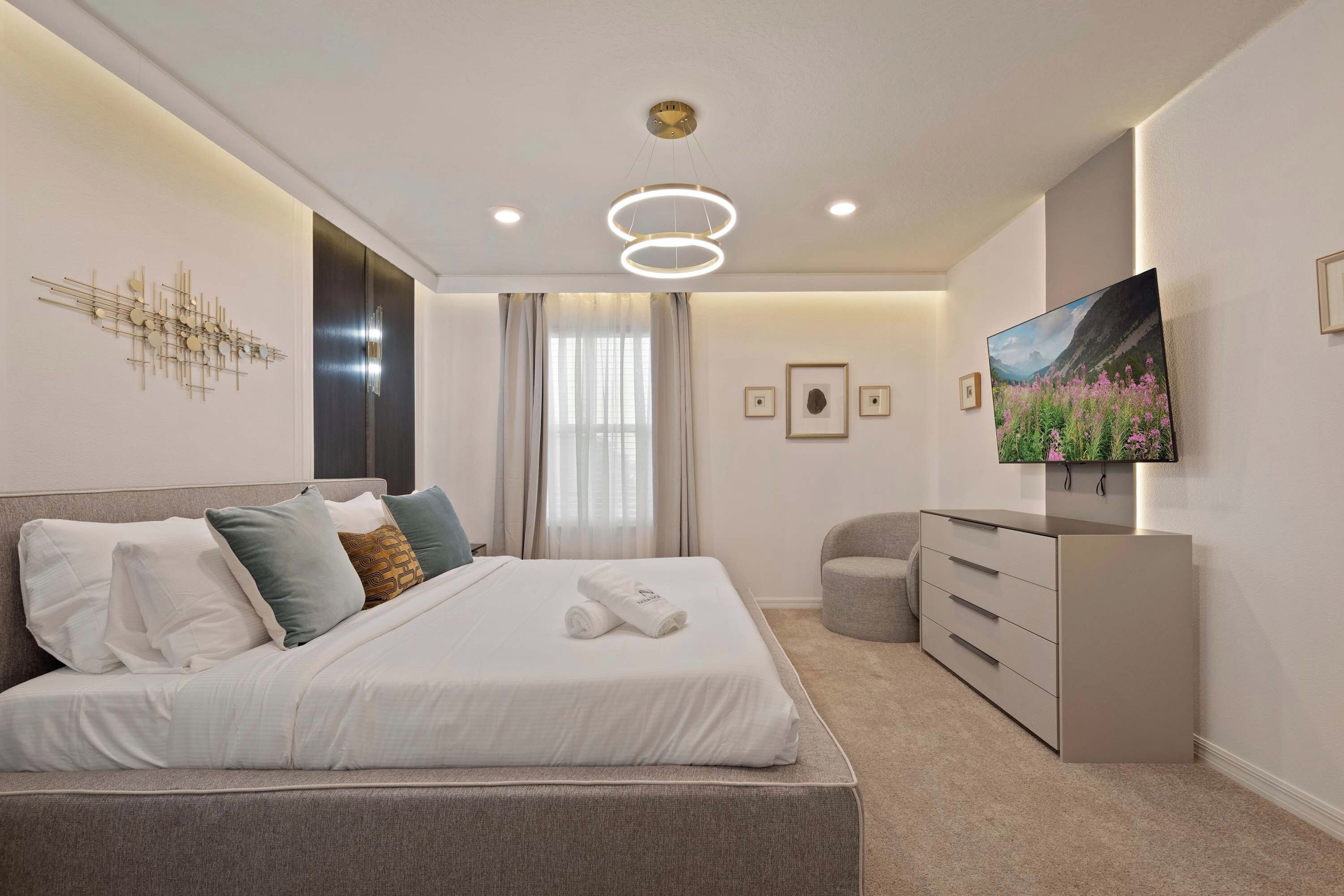 A modern bedroom with a large bed, a dresser, a television, and a decorative wall piece.