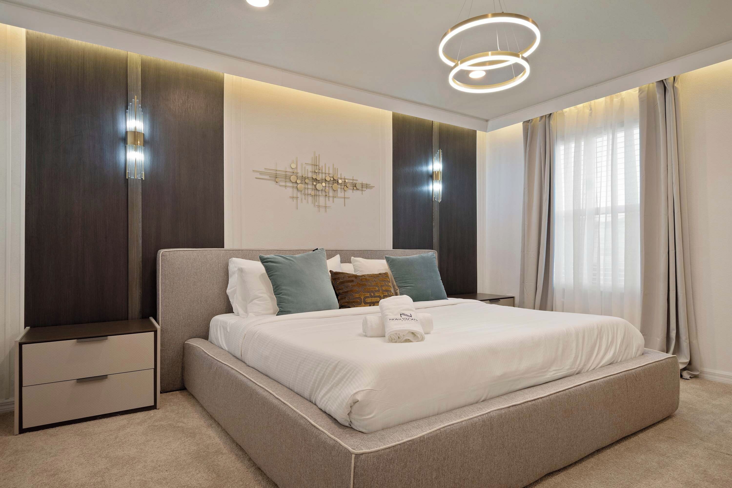 Une chambre à coucher moderne avec un grand lit, des tables de chevet, un luminaire fixé au mur et un élément décoratif mural.
