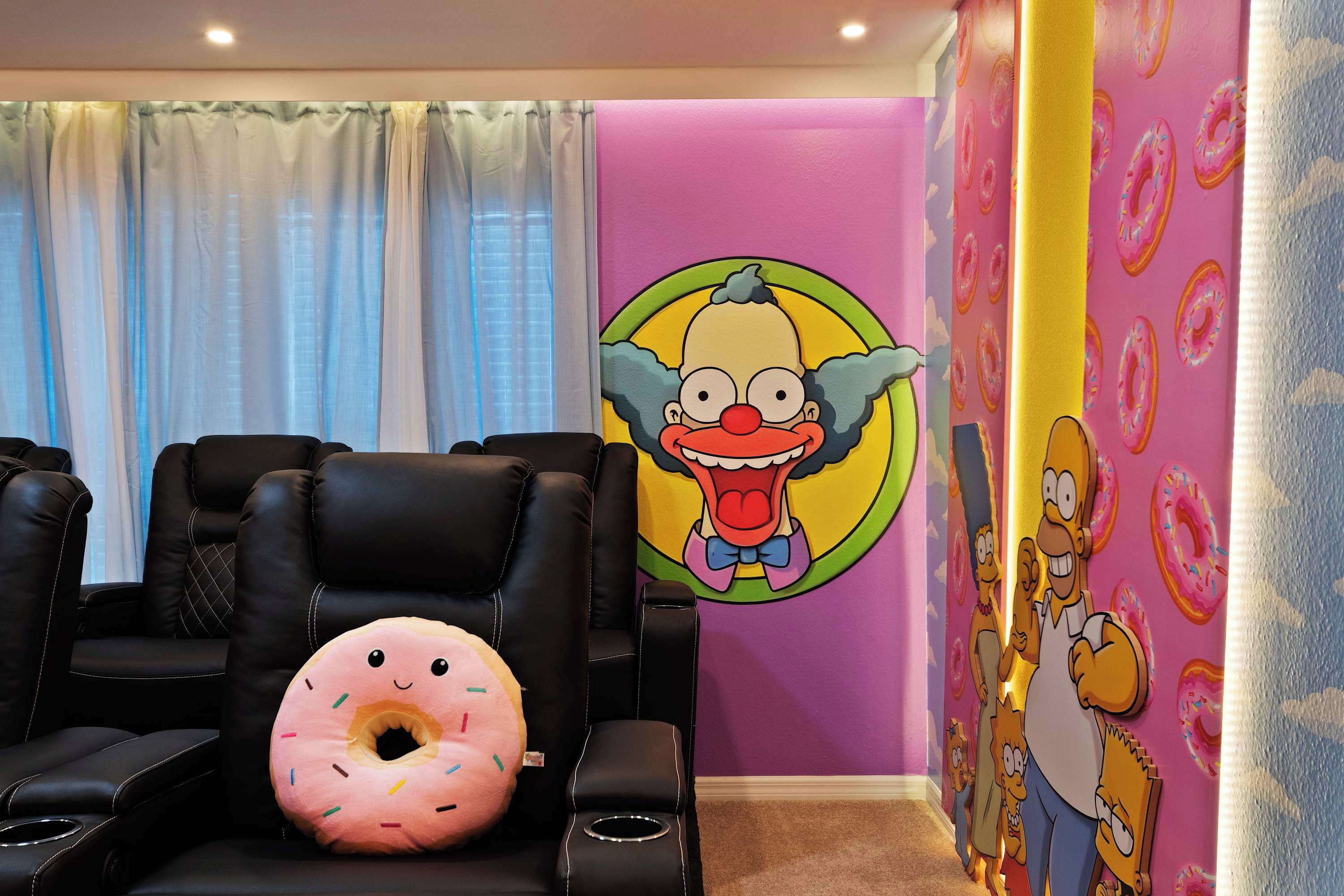 Une pièce avec des fauteuils inclinables en cuir noir, un coussin rose en forme de beignet et une fresque murale représentant un personnage de dessin animé.