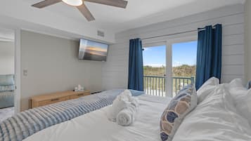 A bedroom with a bed, a ceiling fan, a TV, and a view of the outdoors.
