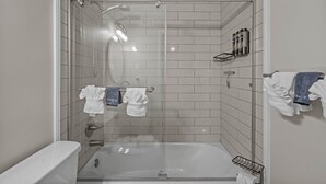 Un baño moderno con ducha de vidrio, bañera y toallero con varias toallas.