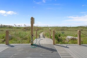 A wooden boardwalk leading to a beach with a rope barrier and a green hose on the ground.