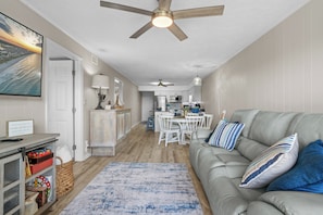A spacious living room with a gray sofa, a blue and white rug, and a ceiling fan.