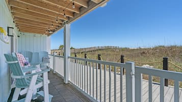 A wooden deck with a white railing, green chairs, and a view of the beach.