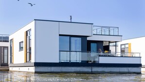 A modern floating house with a balcony, large windows, and a clear sky. - Coastal Comfort With Terrace (Ribnitz-Damgarten)