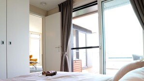 A hotel room with a bed, a desk, and a view of the outside balcony. - Coastal Comfort With Terrace (Ribnitz-Damgarten)