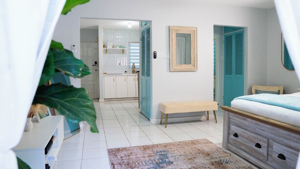 A bedroom with a bed, a bench, a large mirror, and a view into the kitchen. - Serene Super Studio Apartment with porch in Kingston (Kingston)