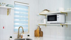 A modern kitchen with white cabinetry, a stainless steel sink, a microwave, and a window with blinds. - Serene Super Studio Apartment with porch in Kingston (Kingston)
