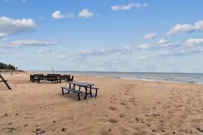 Een strand met een picknicktafel en banken, een heldere lucht en de oceaan op de achtergrond.