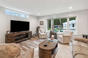 Een ruime woonkamer met een grote flatscreen-tv, comfortabele zithoek en grote ramen met uitzicht op het landschap.