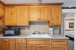 Een kleine keuken met houten kastjes, een magnetron, een spoelbak en een koffiezetapparaat.