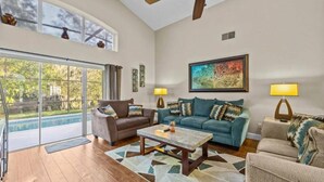 A spacious living room with a large glass door leading to an outdoor area, a ceiling fan, and a painting on the wall.