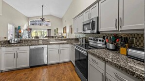 A modern kitchen with granite countertops, stainless steel appliances, and white cabinetry.