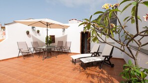 A patio with a round table and chairs, a large umbrella, and a potted plant. - Home2Book La Casita del Muelle (Garachico)