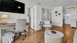 A modern living room with a desk, a comfortable chair, a round coffee table, and a television. - Carolina Beach Retreat | Pool, Ocean View, Beach Access & Stylish Decor (Carolina Beach)