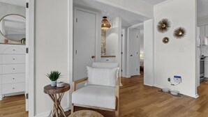 A modern living room with a white sofa, a small round table with a plant, and a wooden floor. - Carolina Beach Retreat | Pool, Ocean View, Beach Access & Stylish Decor (Carolina Beach)