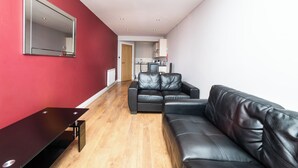 A modern living room with a black leather sofa, a wooden coffee table, and a red accent wall. - 2 Bedroom Apartrment (Newcastle-upon-Tyne)