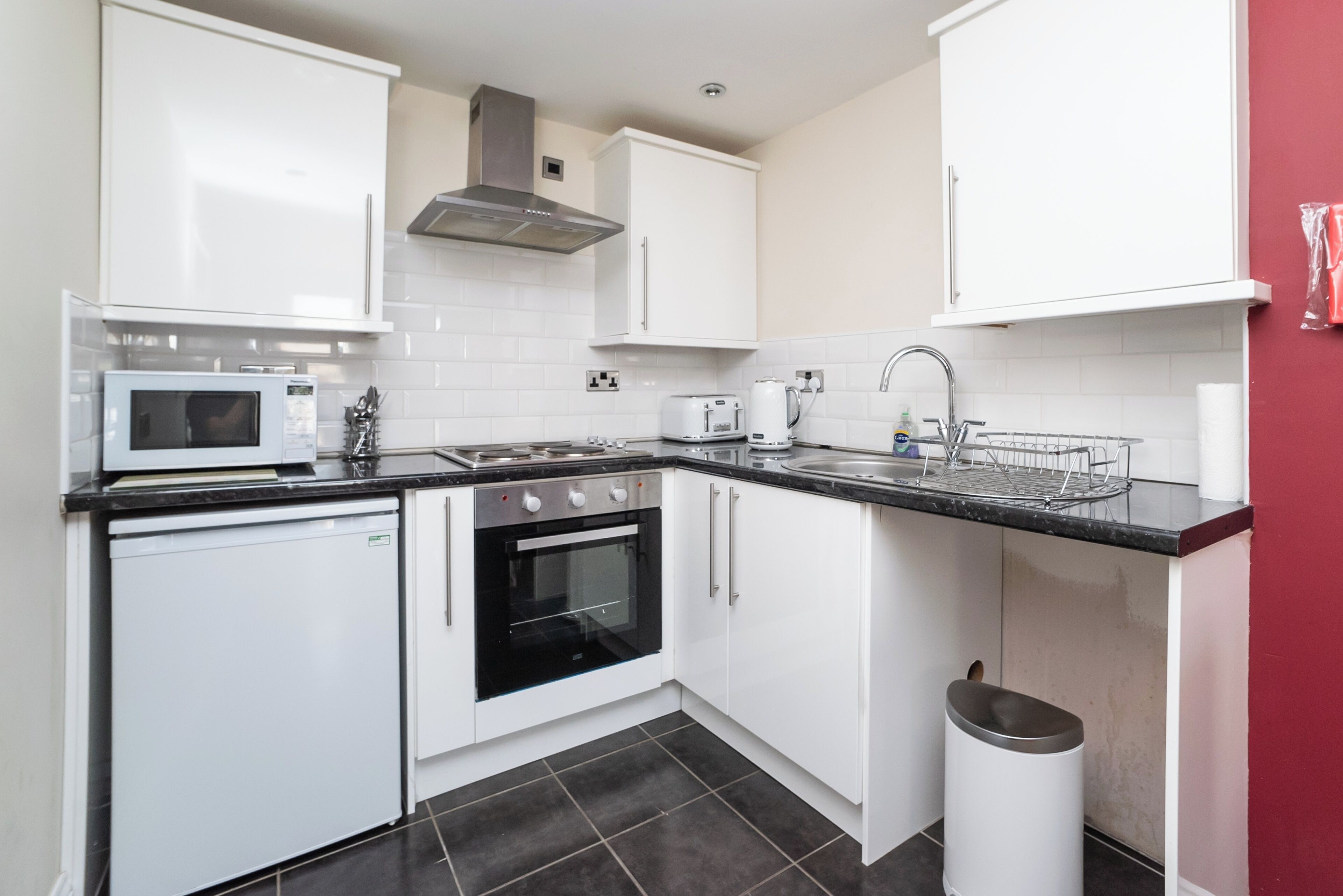 A compact kitchen with white cabinets, a microwave, a toaster, a kettle, and a sink.