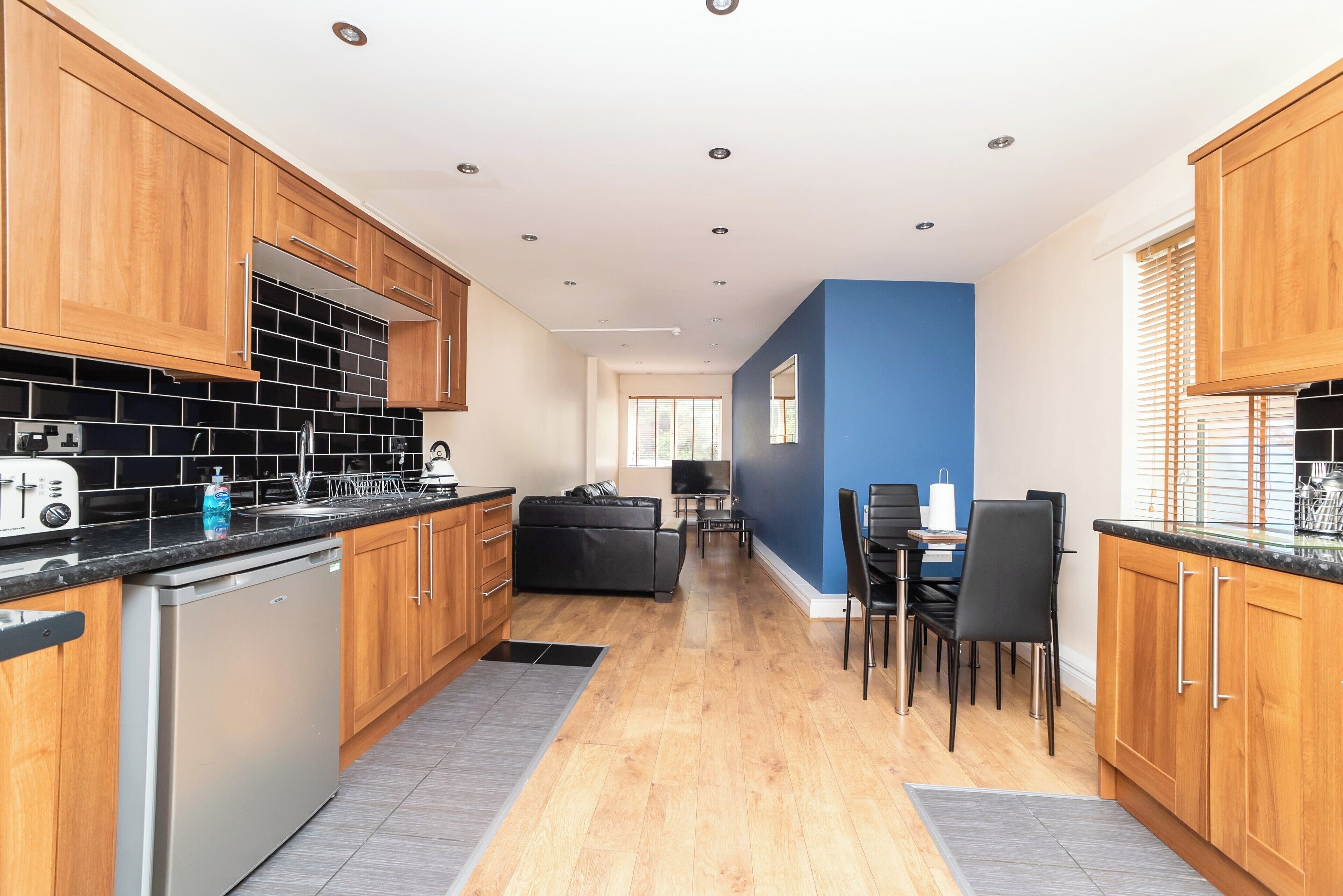A modern kitchen with wooden cabinets, a black tiled backsplash, and a stainless steel dishwasher.