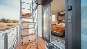 A modern bedroom with a wooden deck, a glass door leading to a balcony, and a bed with a brown blanket.